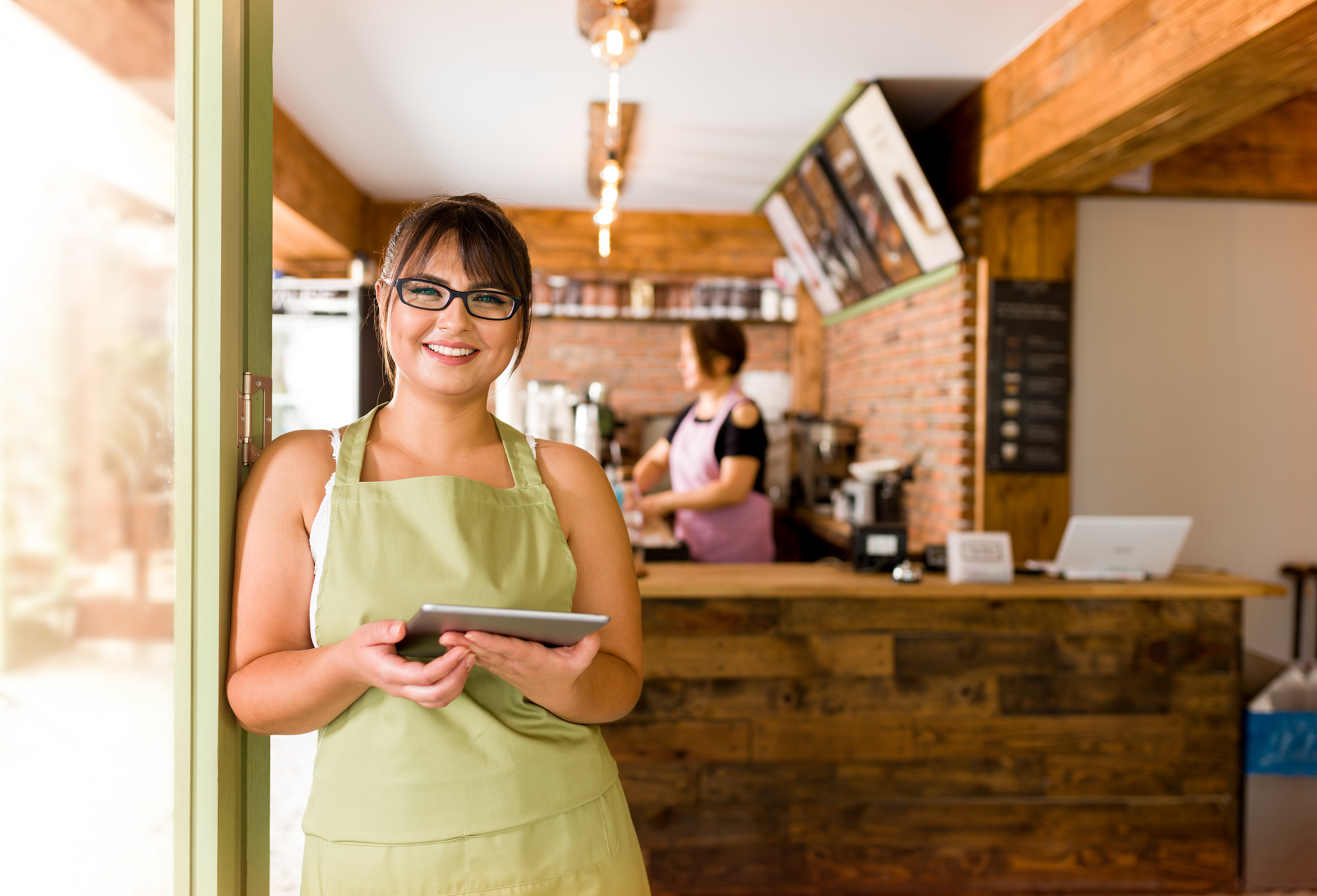 Cafe owner stands in doorway holding tablet