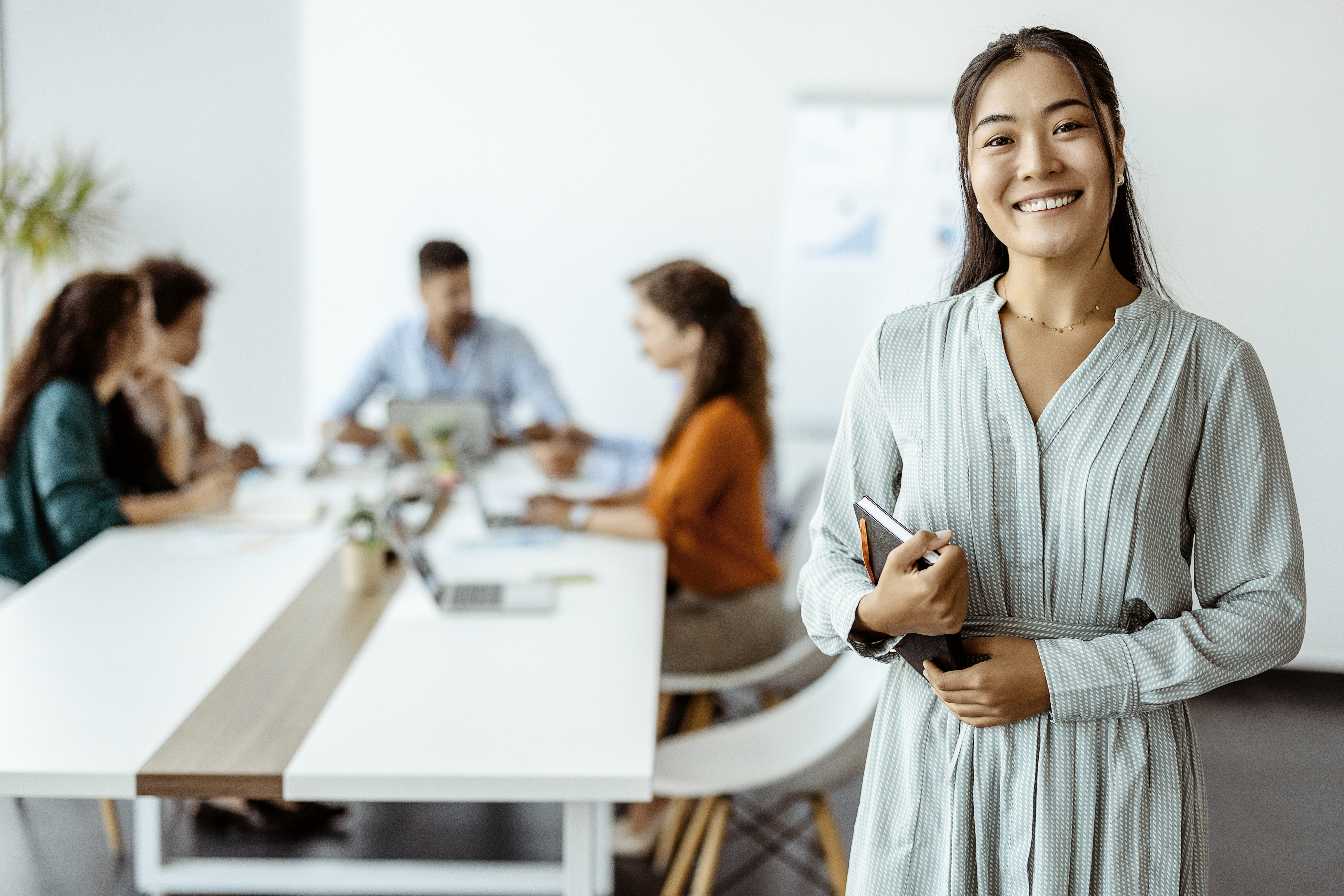 Confident young businesswoman standing smiling at the camera in a boardroom with colleagues in the background